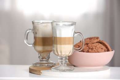 Photo of Aromatic latte macchiato in glasses and chocolate cookies on white table against light background