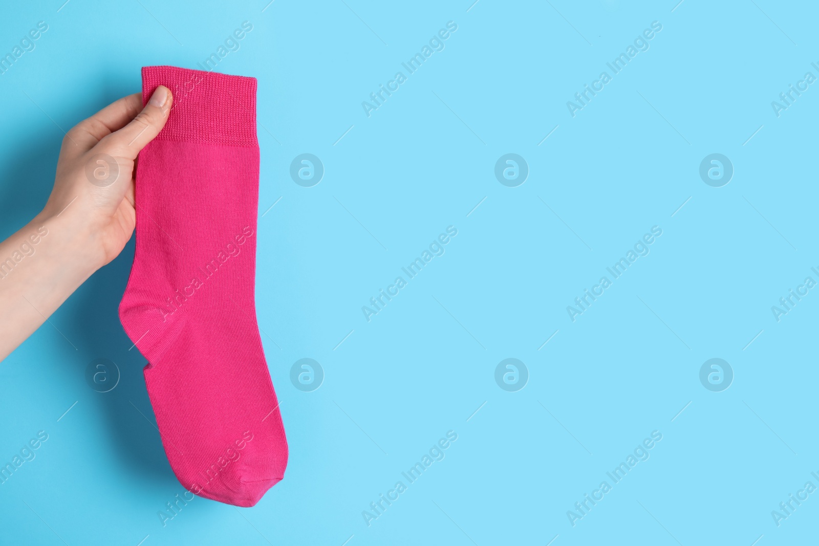 Photo of Woman holding pink sock on light blue background, closeup. Space for text
