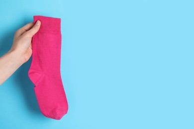 Photo of Woman holding pink sock on light blue background, closeup. Space for text