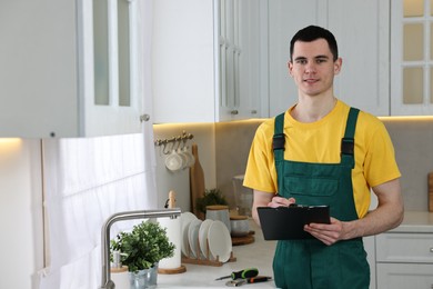 Smiling plumber with clipboard near faucet in kitchen