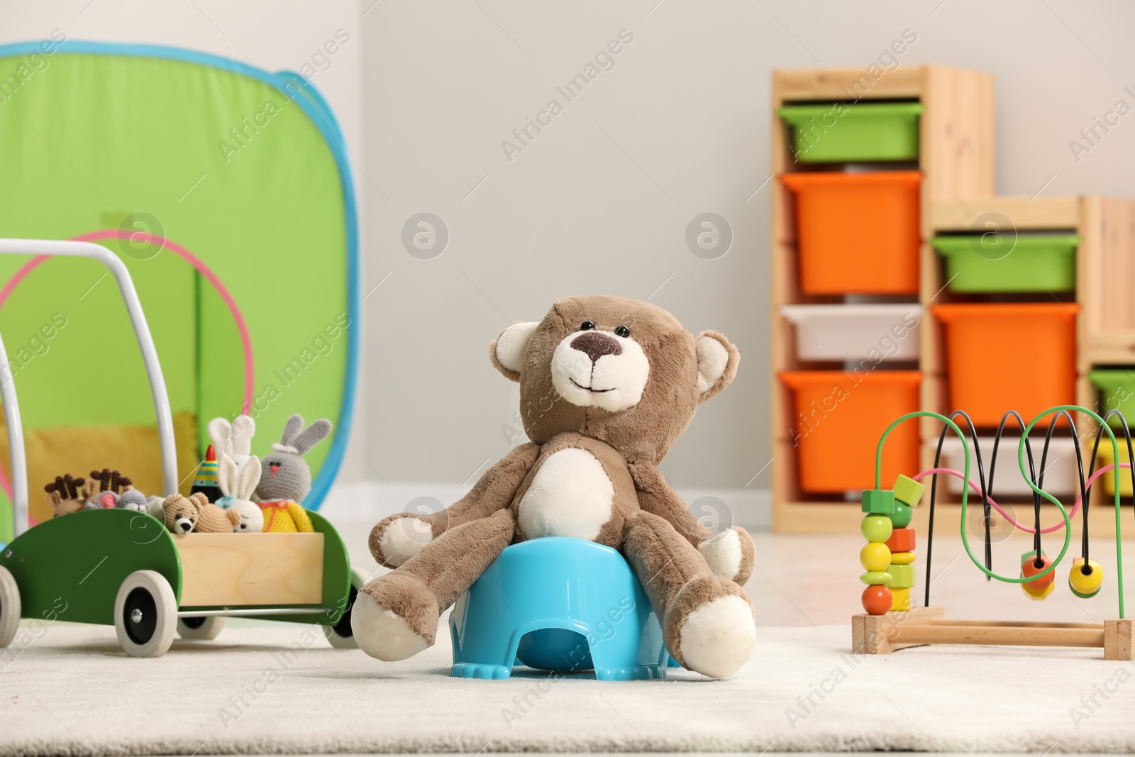 Photo of Cute teddy bear on light blue baby potty on floor in room. Toilet training