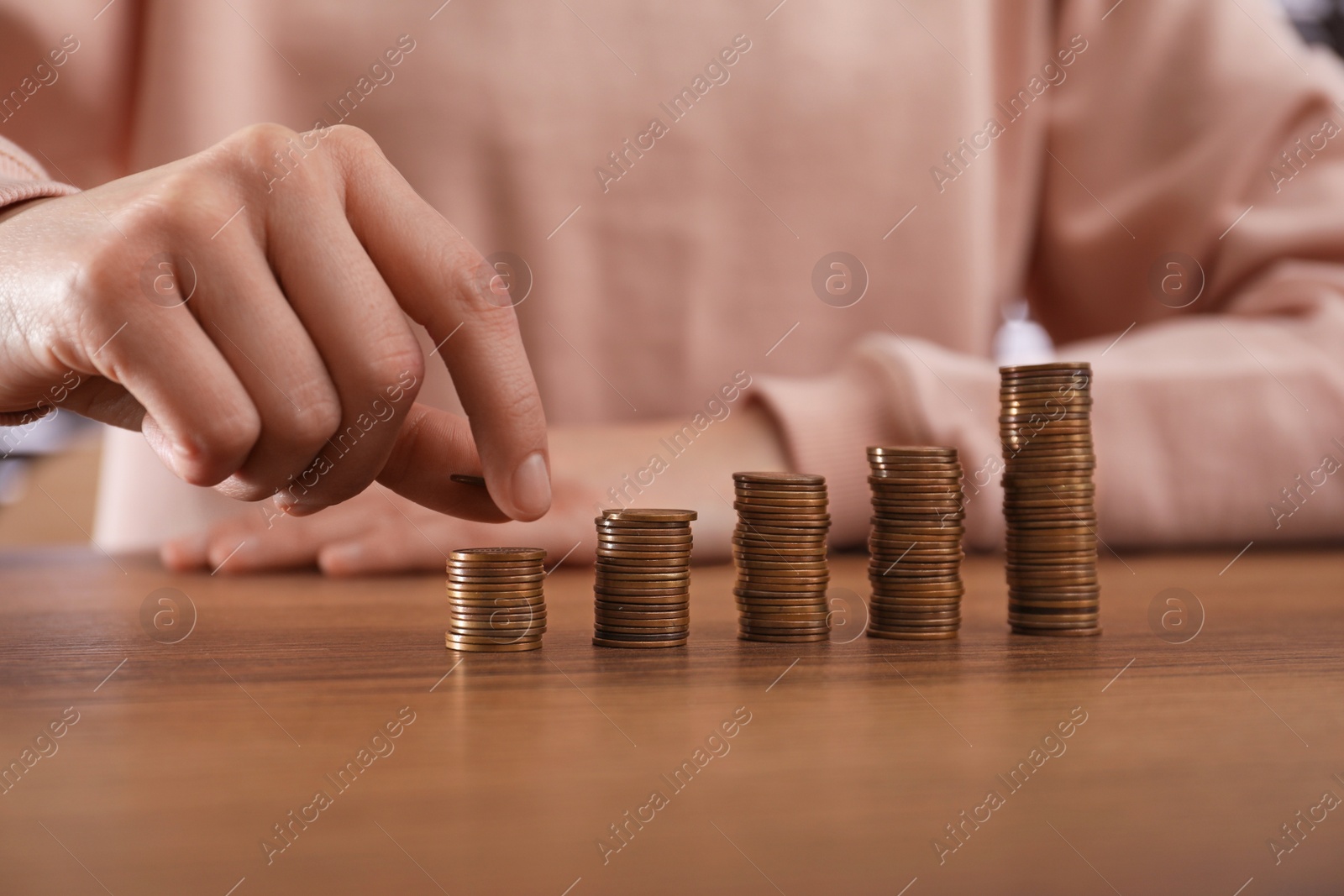 Photo of Woman stacking coins at wooden table, closeup