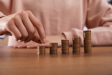 Woman stacking coins at wooden table, closeup