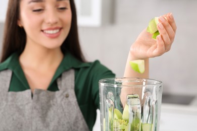 Photo of Woman adding apples into blender with ingredients for smoothie in kitchen, focus on hand
