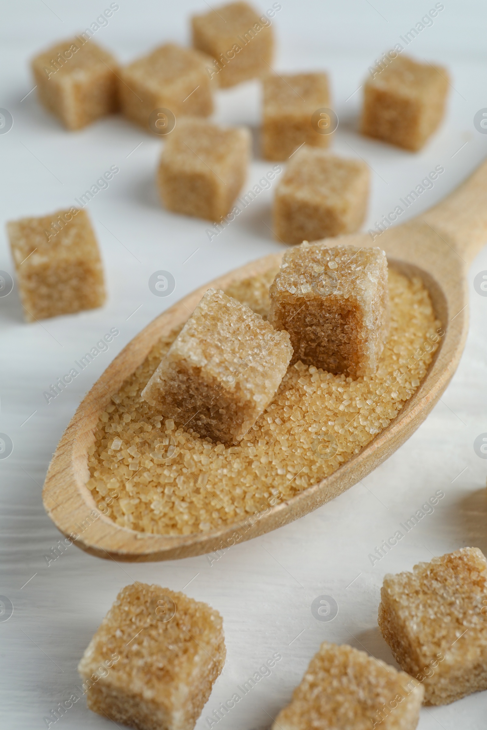 Photo of Brown sugar cubes in spoon on white wooden table, closeup