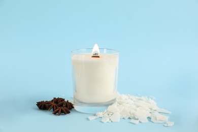 Photo of Burning soy candle, wax flakes and anise stars on light blue background