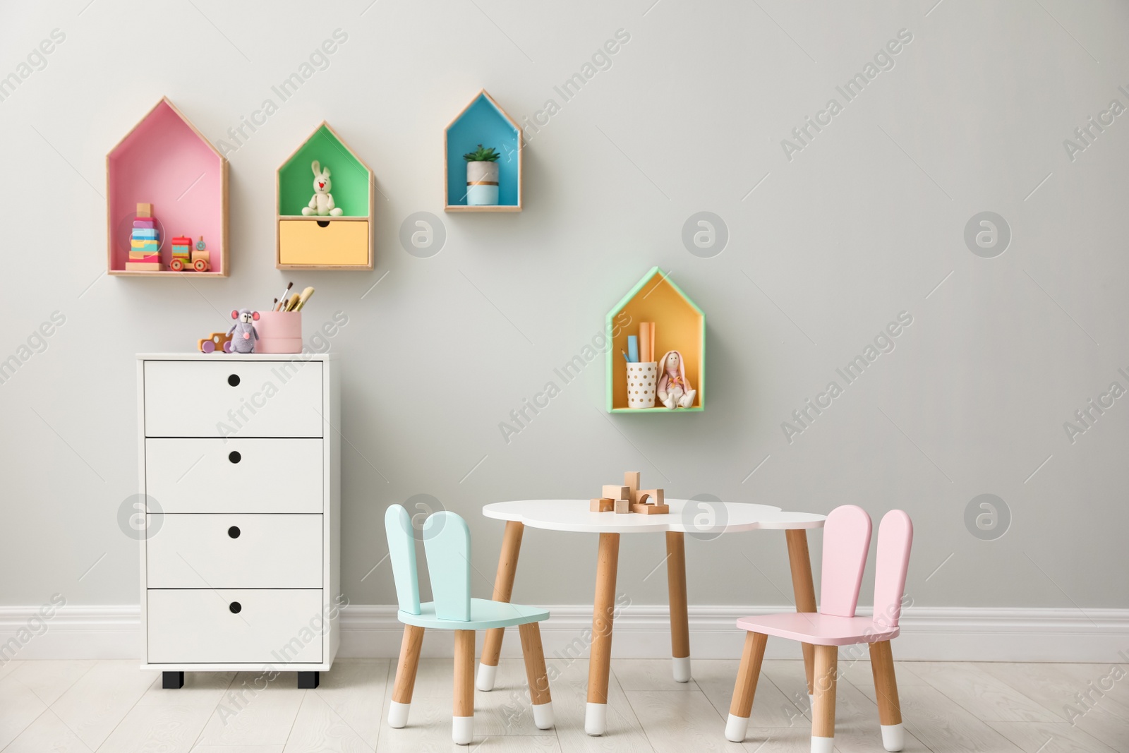 Photo of House shaped shelves and little table with chairs in children's room. Interior design