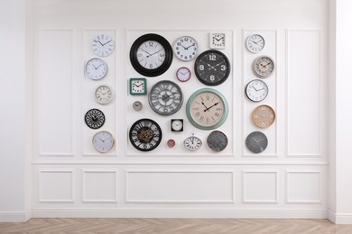 Photo of Collection of different clocks hanging on white wall in room