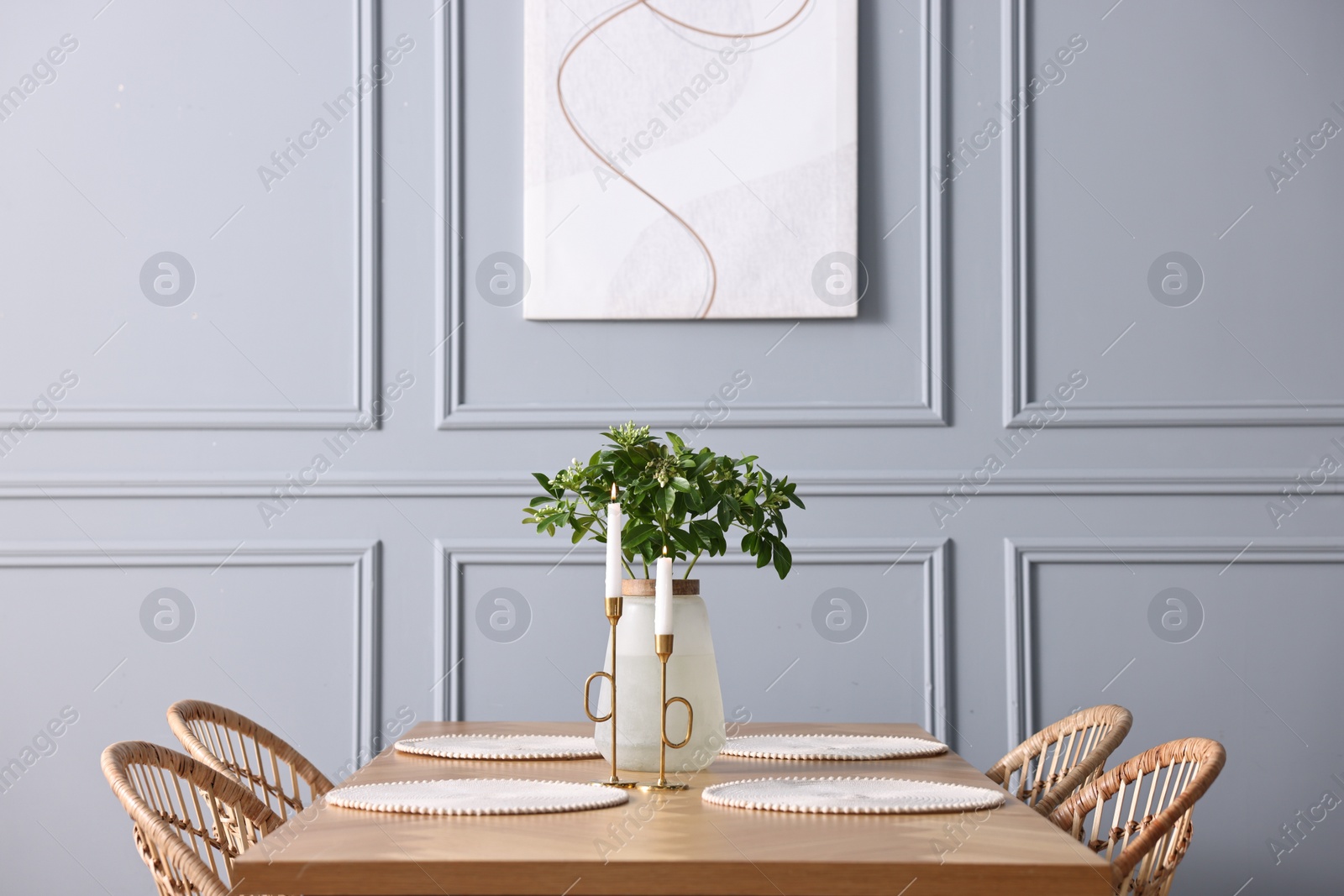 Photo of Rattan chairs, table, burning candles and vase with green branches in stylish dining room