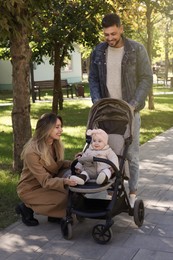 Happy parents walking with their baby in stroller at park on sunny day