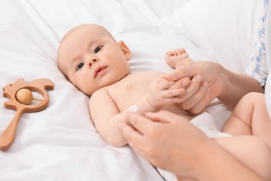 Woman applying body cream onto baby`s skin on bed, closeup