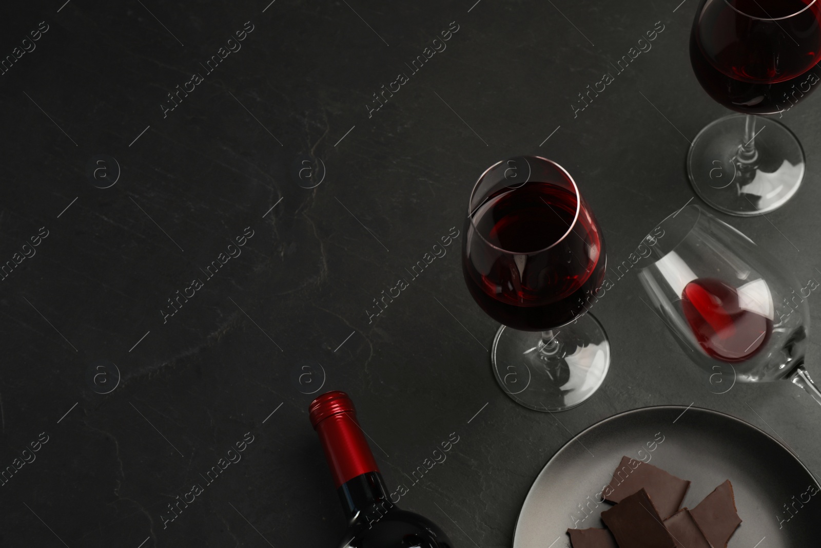 Photo of Composition with tasty red wine and chocolate on black table, above view. Space for text