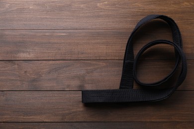 Photo of Black belt on wooden background, top view with space for text. Oriental martial arts