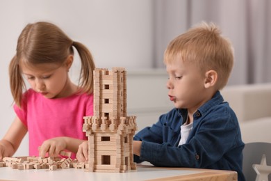 Photo of Little girl and boy playing with wooden tower at table indoors. Children's toy