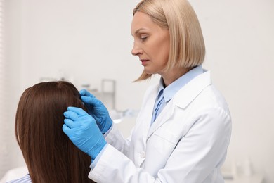 Trichologist in gloves examining patient`s hair in clinic