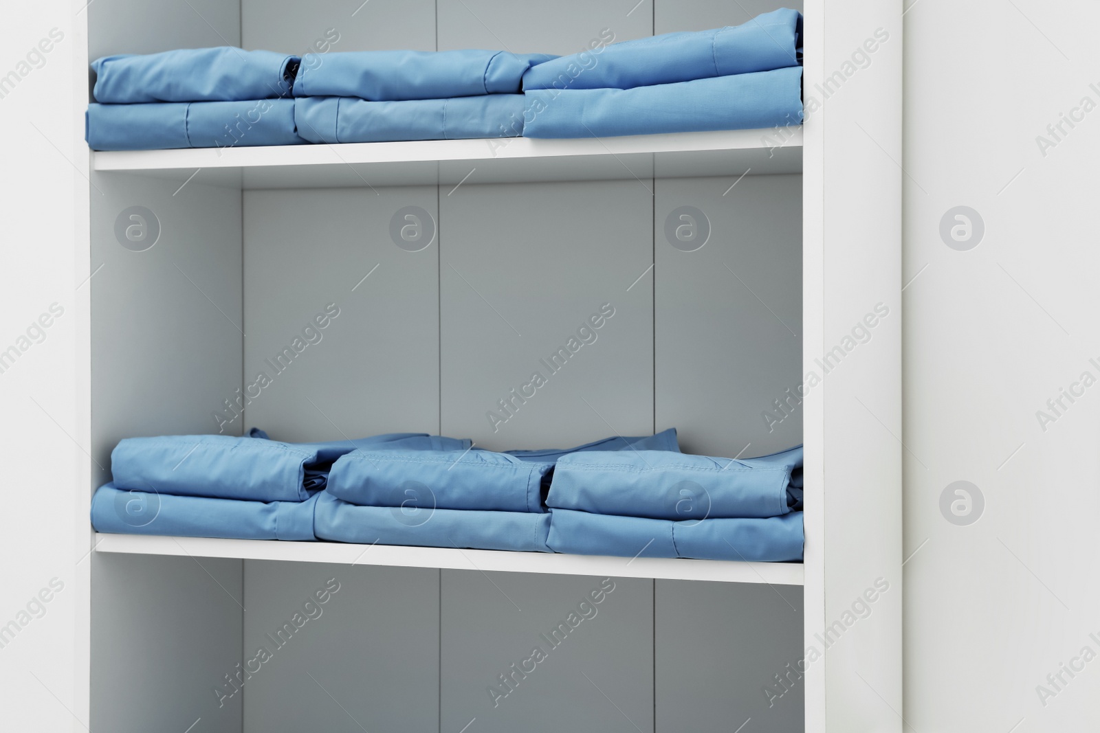 Photo of Light blue medical uniforms on white rack