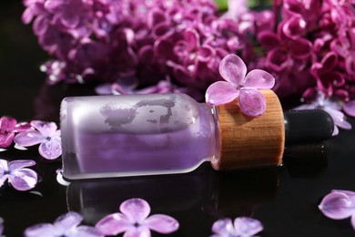 Photo of Bottle with essential oil, lilac flowers and water on black surface, closeup