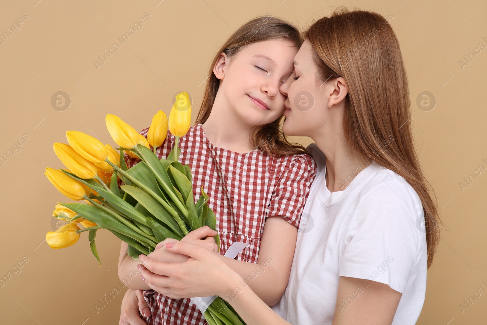 Photo of Mother and her cute daughter with bouquet of yellow tulips on beige background