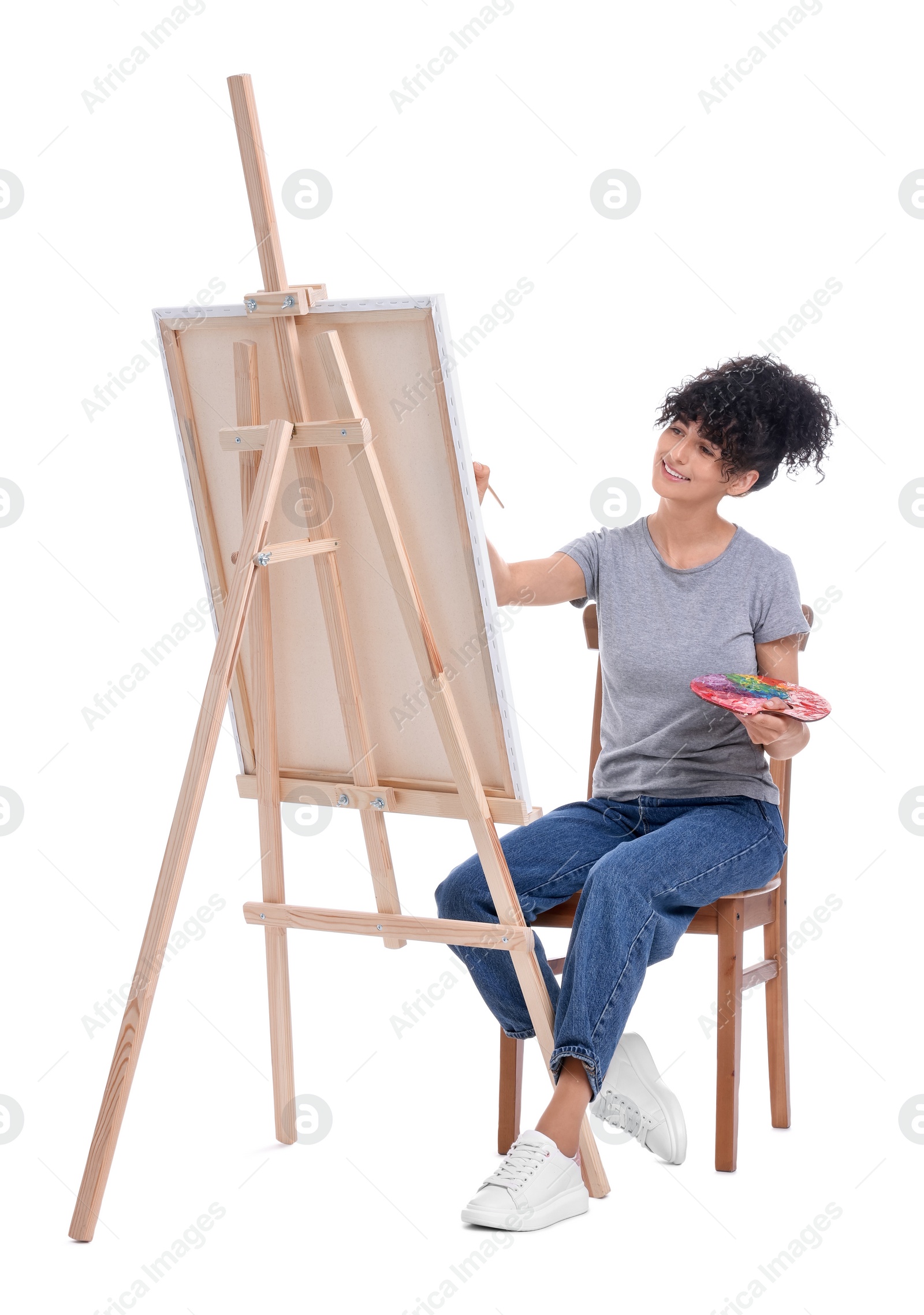 Photo of Young woman painting on easel with canvas against white background