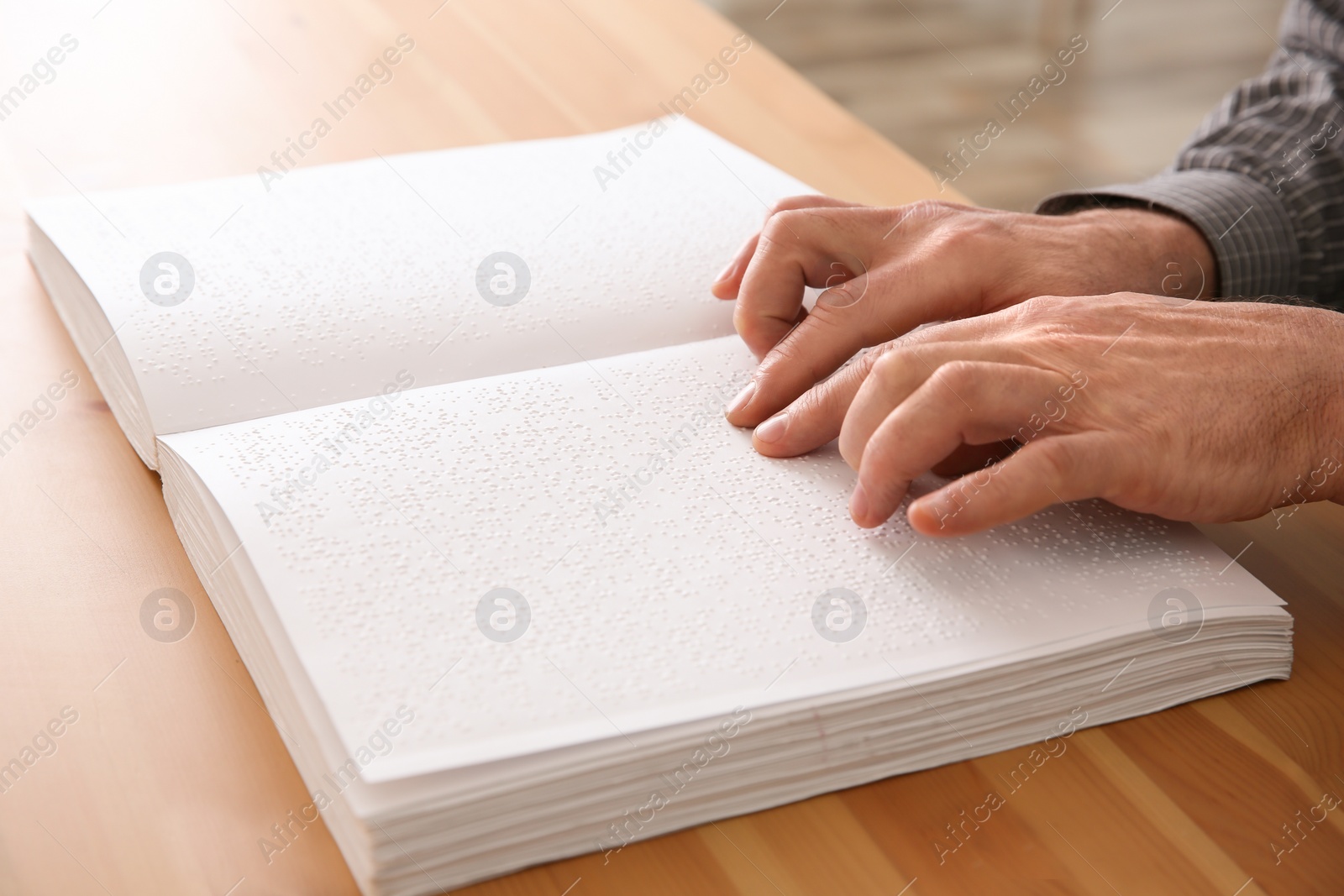 Photo of Blind man reading book written in Braille at table, closeup