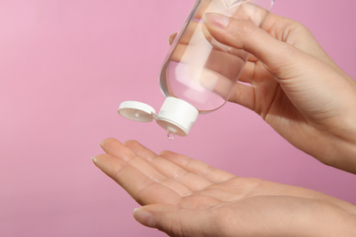 Woman applying antiseptic gel on pink background, closeup