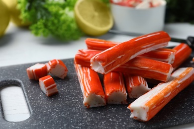 Photo of Delicious crab sticks on black board, closeup