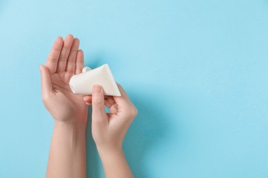 Woman applying cosmetic cream from tube onto her hand on light blue background, top view. Space for text