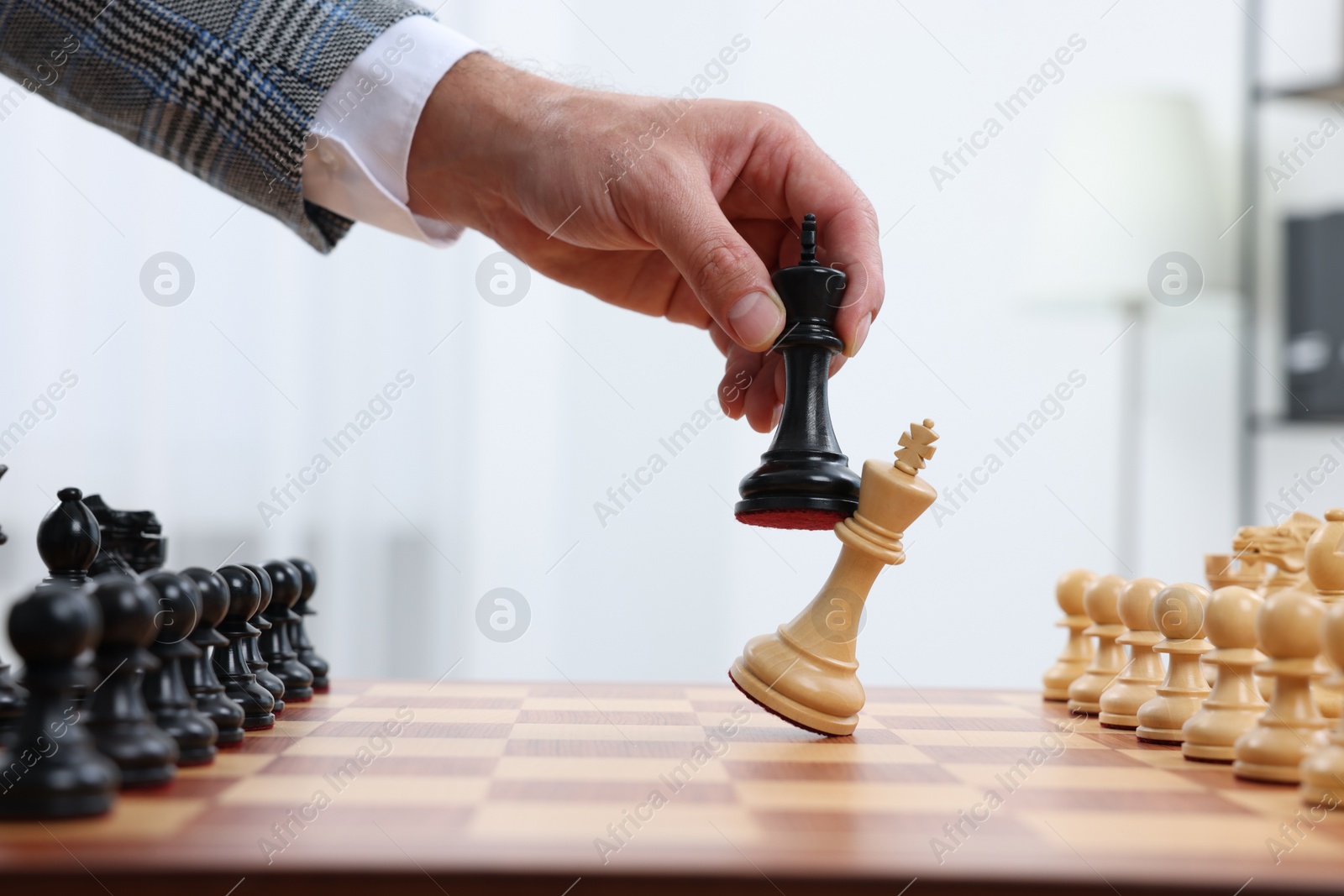 Photo of Man with king game piece playing chess at checkerboard indoors, closeup