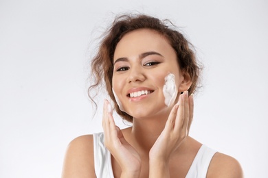 Beautiful young woman with problem skin applying anti acne cream on light background