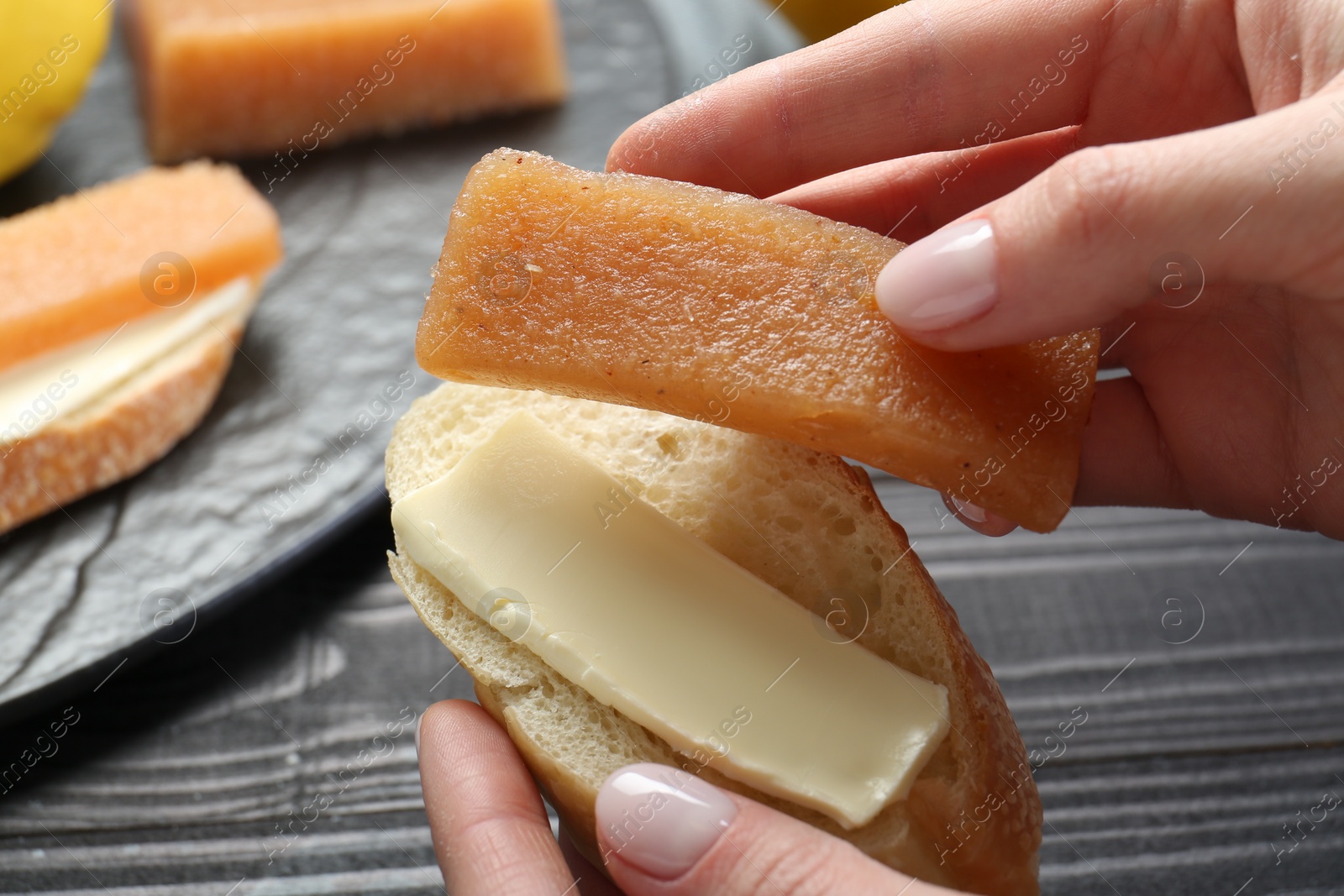 Photo of Woman making sandwich with quince paste at black wooden table, closeup