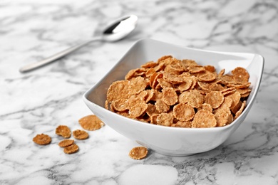 Photo of Bowl with cornflakes on marble table. Whole grain cereal for breakfast