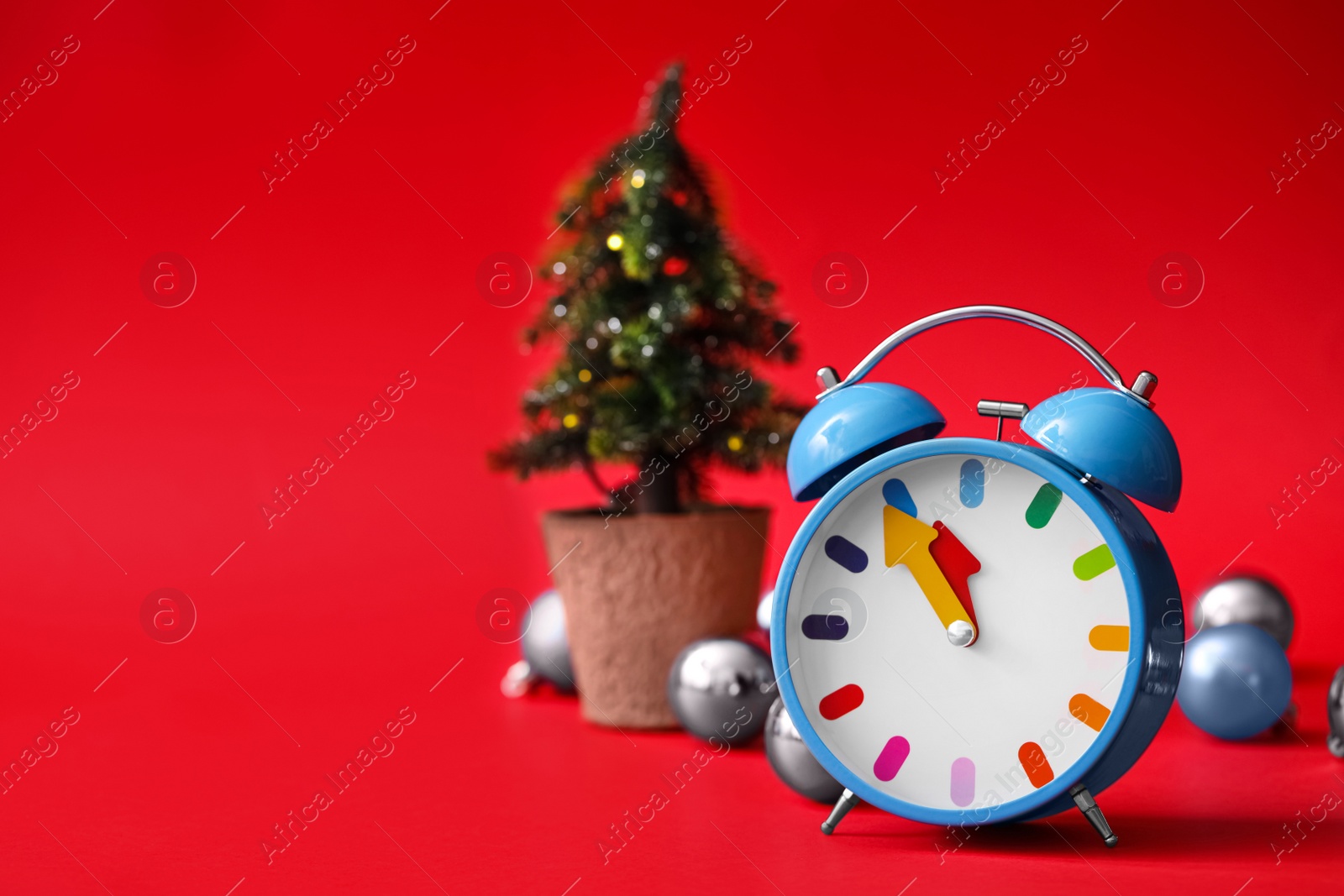 Photo of Alarm clock and festive decor on red background, space for text. New Year countdown