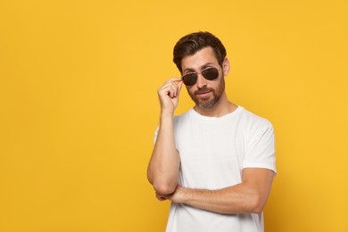 Photo of Portrait of bearded man with stylish sunglasses on orange background. Space for text
