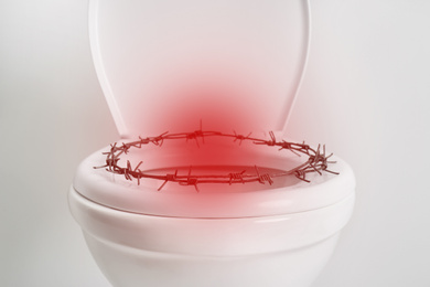 Hemorrhoid concept. Toilet bowl with barbed wire on white background