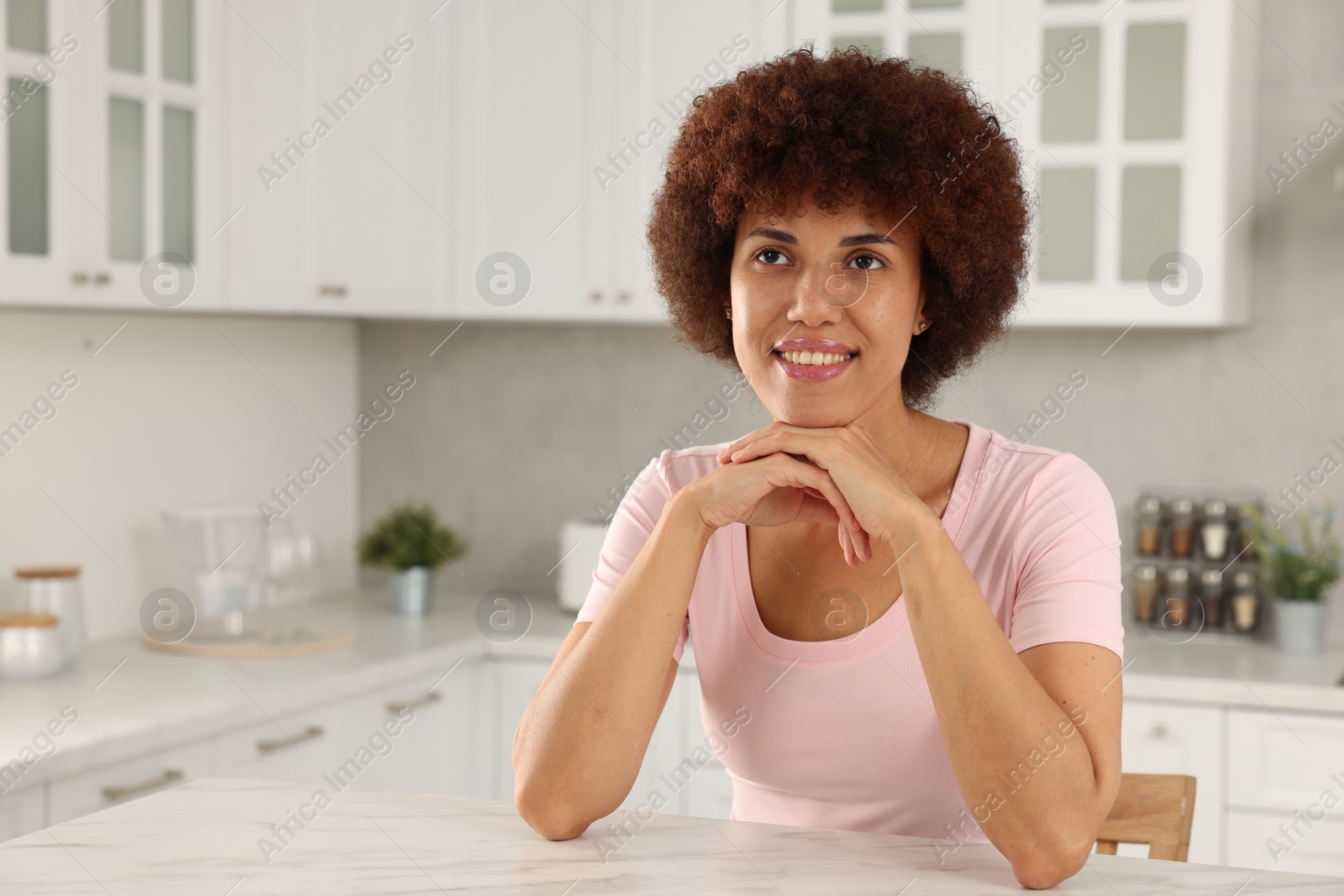 Photo of Happy young woman sitting at table in kitchen. Space for text