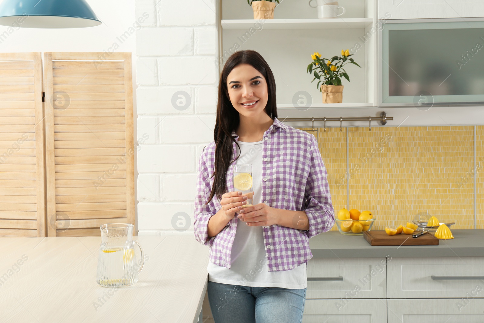 Photo of Beautiful young woman with lemon water in kitchen