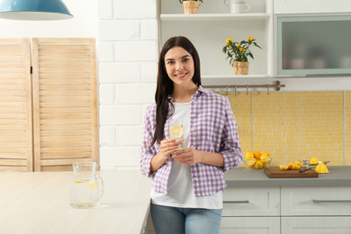 Beautiful young woman with lemon water in kitchen