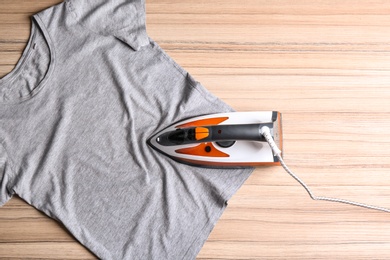 Photo of Flat lay composition with modern electric iron and t-shirt on wooden table. Space for text