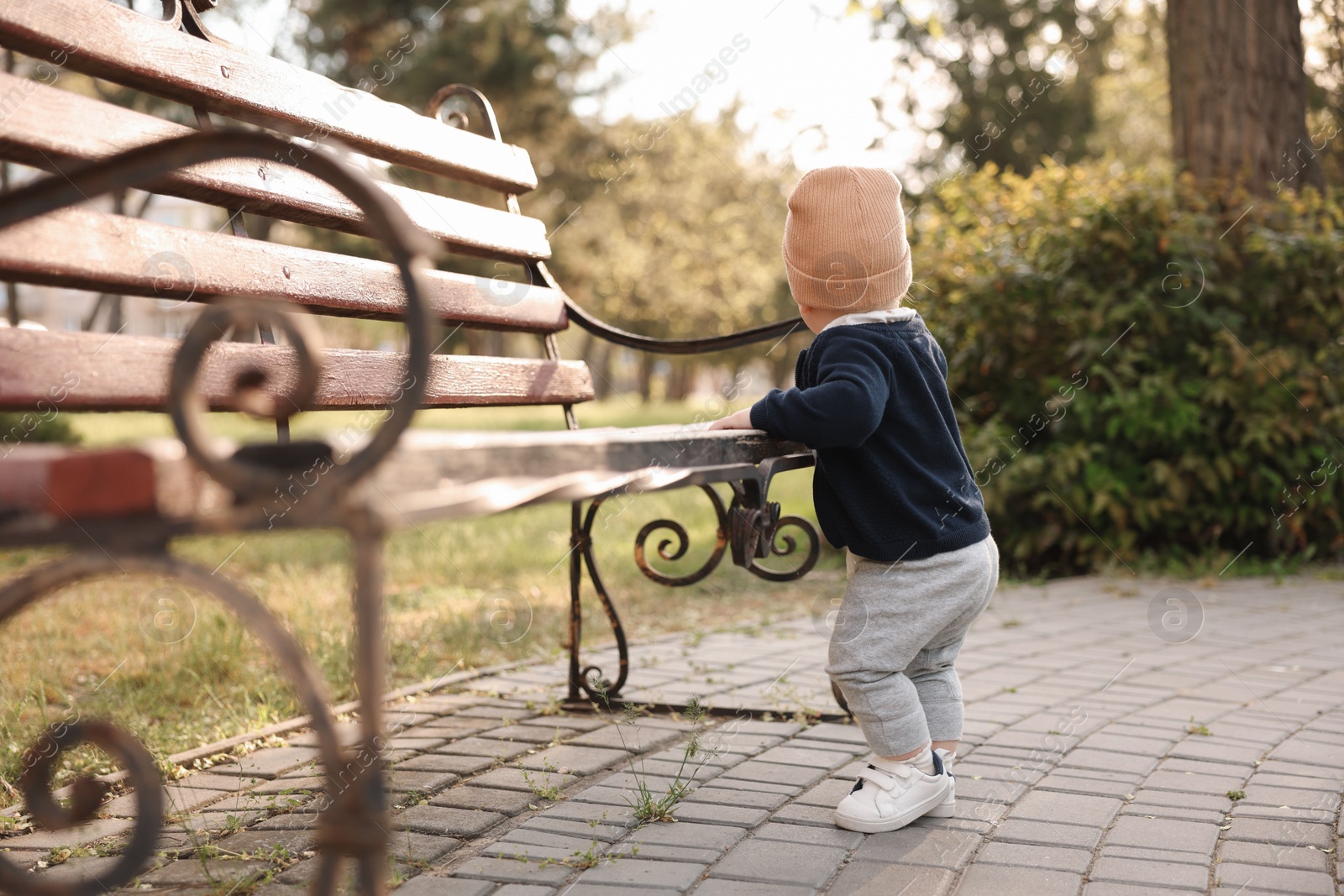 Photo of Little baby learning to walk near bench in park