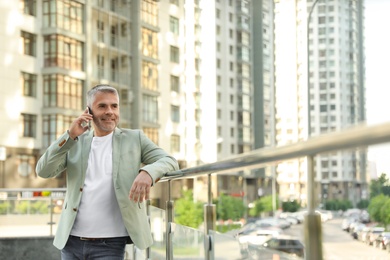 Handsome mature man talking on phone in city center. Space for text