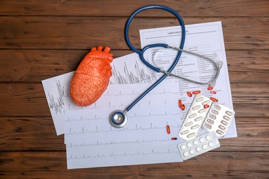 Flat lay composition with stethoscope and pills on wooden background. Cardiology service