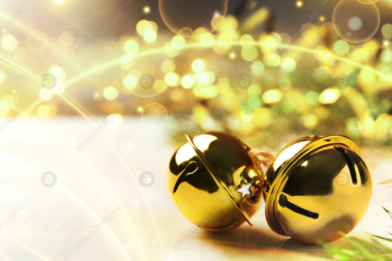 Image of Golden sleigh bells on white table, closeup. Space for text