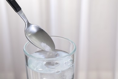 Adding baking soda into glass of water on light background, closeup. Space for text