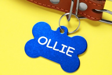 Image of Leather dog collar with blue tag in shape of bone on yellow background, closeup