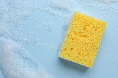 Photo of Yellow sponge with foam on light blue background, top view. Space for text