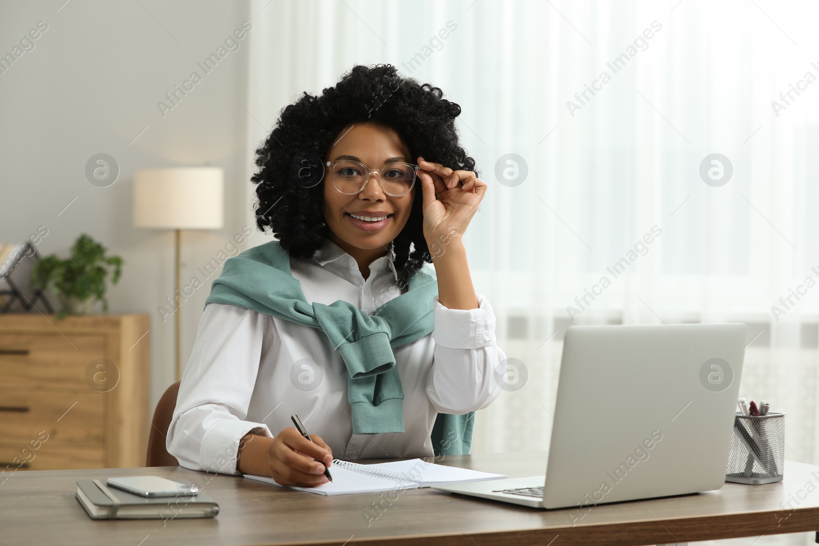 Photo of Happy young woman using laptop at wooden desk indoors