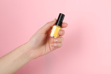 Photo of Woman holding nail polish on pink background, closeup