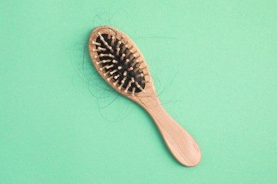 Photo of Wooden brush with lost hair on green background, top view