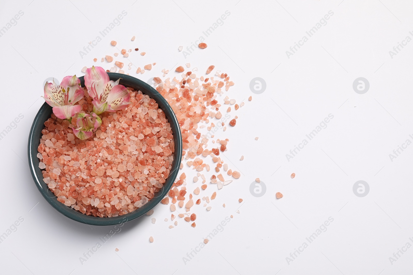 Photo of Natural sea salt and flowers in bowl on white background, top view. Space for text
