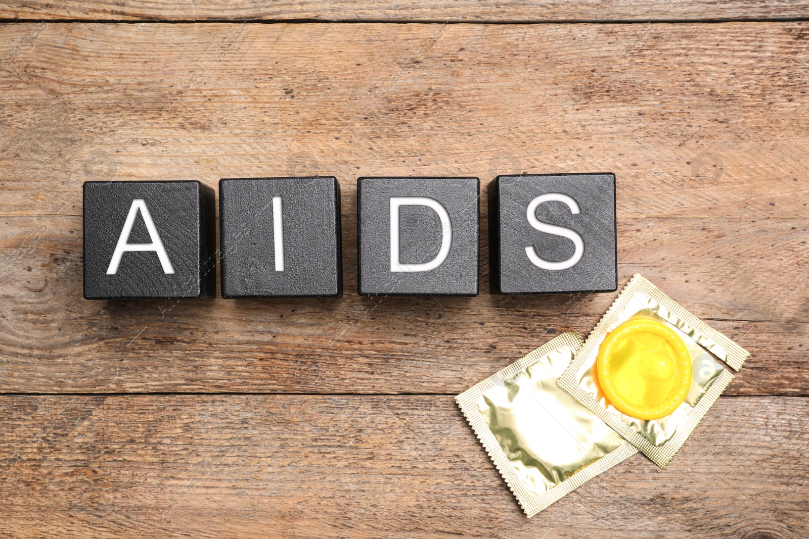 Photo of Word AIDS made with black cubes and shiny condoms on wooden background, flat lay. Safe sex